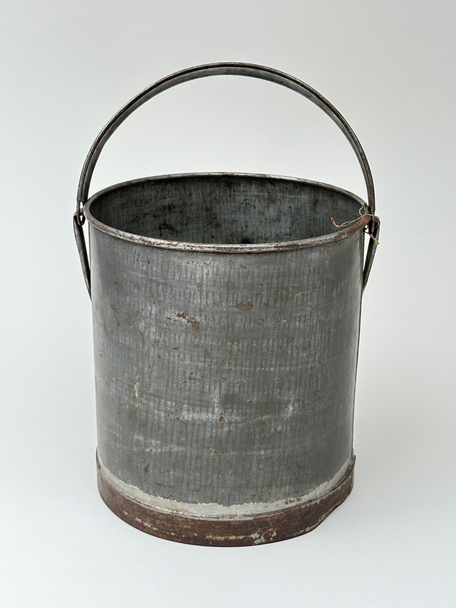 Mjölkspann. Av bleckplåt, cylinder, med hank av kantfalsad bleckplåt. Rullad överkant och förstärkt nederkant med bandplåt, nu rostig. Pålödda öron av bleckplåt. 
