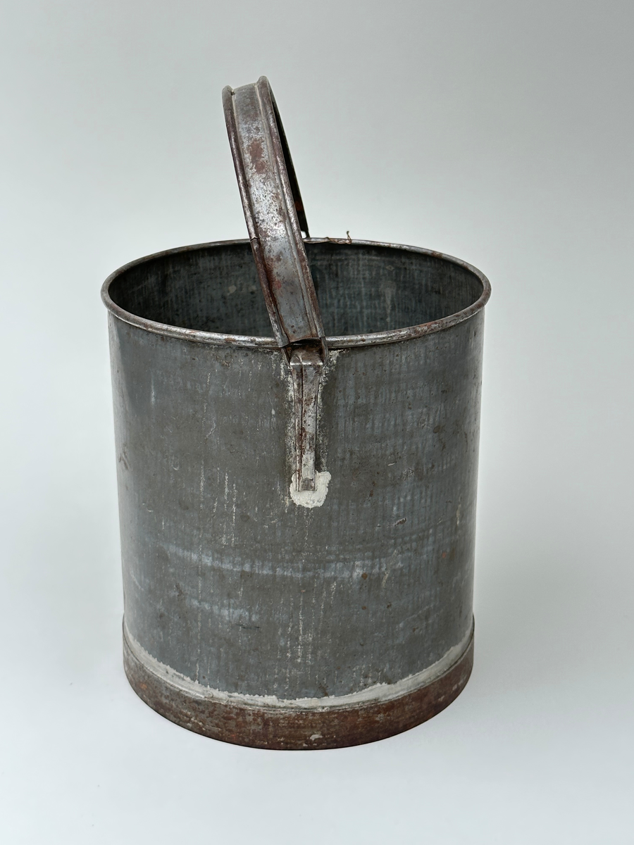 Mjölkspann. Av bleckplåt, cylinder, med hank av kantfalsad bleckplåt. Rullad överkant och förstärkt nederkant med bandplåt, nu rostig. Pålödda öron av bleckplåt. 