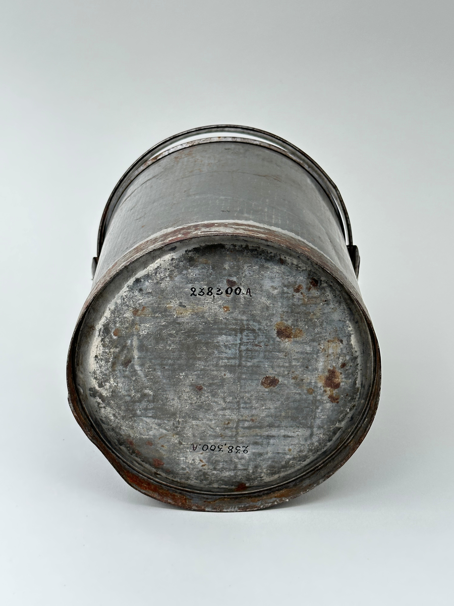 Mjölkspann. Av bleckplåt, cylinder, med hank av kantfalsad bleckplåt. Rullad överkant och förstärkt nederkant med bandplåt, nu rostig. Pålödda öron av bleckplåt. 