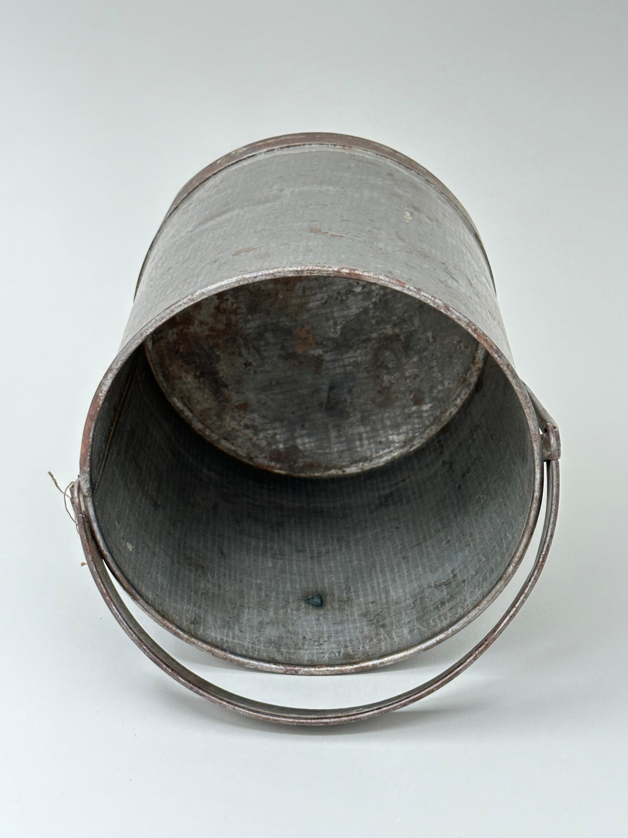 Mjölkspann. Av bleckplåt, cylinder, med hank av kantfalsad bleckplåt. Rullad överkant och förstärkt nederkant med bandplåt, nu rostig. Pålödda öron av bleckplåt. 