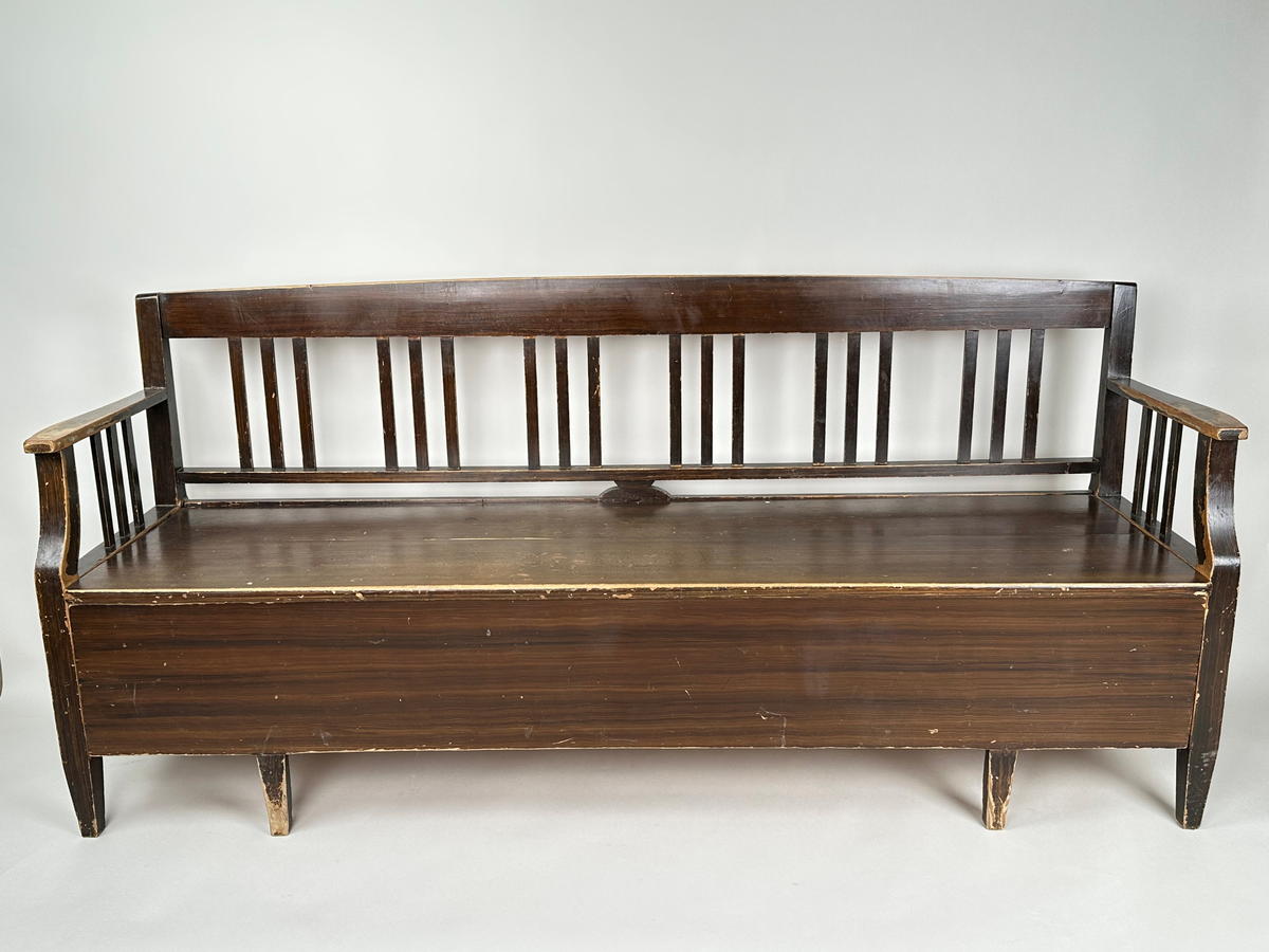 Kökssoffa i ådringsmålat trä. Välvd spjälrygg bestående av sex grupper av tre spjälor i varje. Armstöd med tre spjälor samt en svängd främre stolpe som övergår i soffans framben i respektive hörn. Lock bestående av två brädor, avtagbart. Soffan utdragbar, insidan obehandlad. Den utdragbara delen har två lätt konade ben i framkant.