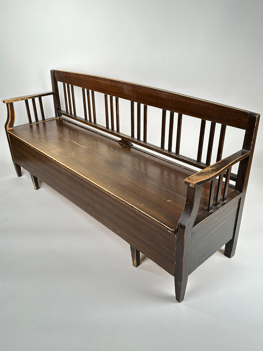 Kökssoffa i ådringsmålat trä. Välvd spjälrygg bestående av sex grupper av tre spjälor i varje. Armstöd med tre spjälor samt en svängd främre stolpe som övergår i soffans framben i respektive hörn. Lock bestående av två brädor, avtagbart. Soffan utdragbar, insidan obehandlad. Den utdragbara delen har två lätt konade ben i framkant.