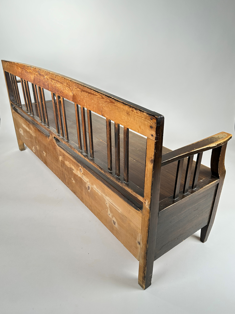 Kökssoffa i ådringsmålat trä. Välvd spjälrygg bestående av sex grupper av tre spjälor i varje. Armstöd med tre spjälor samt en svängd främre stolpe som övergår i soffans framben i respektive hörn. Lock bestående av två brädor, avtagbart. Soffan utdragbar, insidan obehandlad. Den utdragbara delen har två lätt konade ben i framkant.