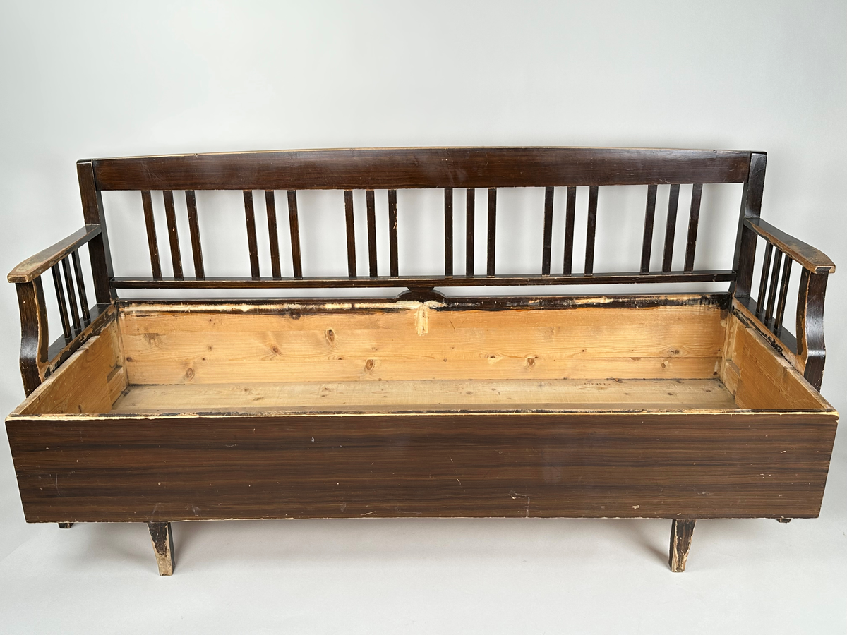 Kökssoffa i ådringsmålat trä. Välvd spjälrygg bestående av sex grupper av tre spjälor i varje. Armstöd med tre spjälor samt en svängd främre stolpe som övergår i soffans framben i respektive hörn. Lock bestående av två brädor, avtagbart. Soffan utdragbar, insidan obehandlad. Den utdragbara delen har två lätt konade ben i framkant.