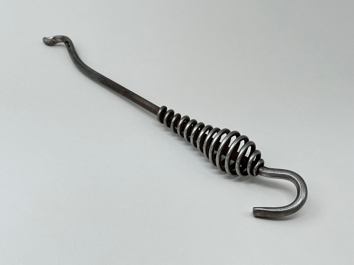 Spiskrok i järn. Med petkrok i ena änden och upphängningskrok i den andra. Handtaget är gjort av en virad ståltråd. 