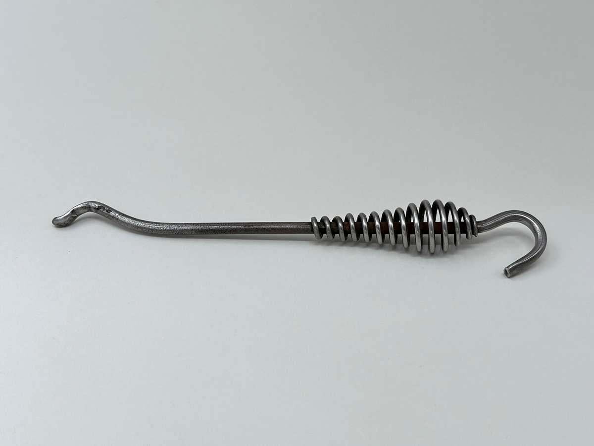 Spiskrok i järn. Med petkrok i ena änden och upphängningskrok i den andra. Handtaget är gjort av en virad ståltråd. 