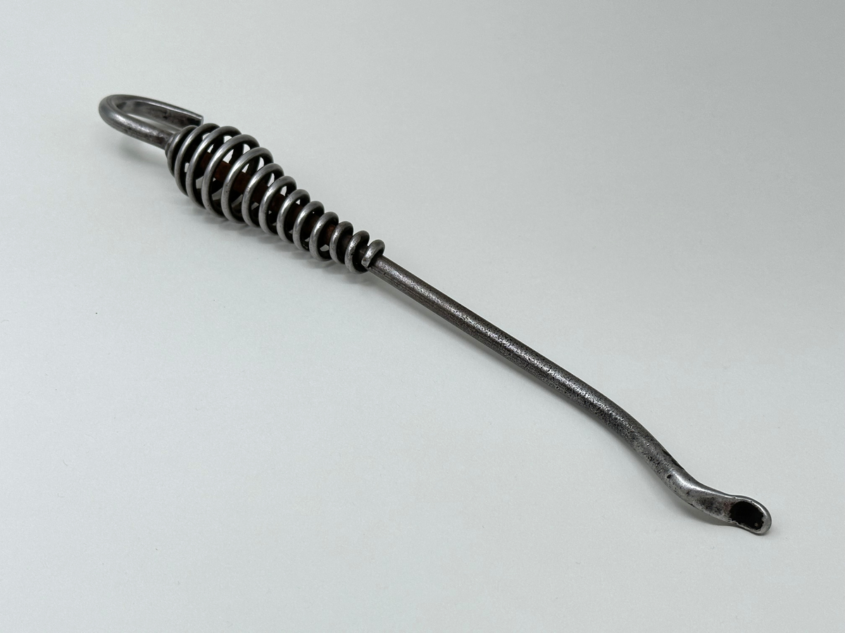 Spiskrok i järn. Med petkrok i ena änden och upphängningskrok i den andra. Handtaget är gjort av en virad ståltråd. 
