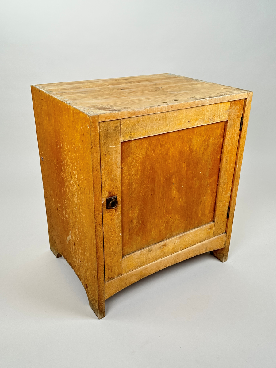 Kommod tillhörande tvättställ. I trä, furu med björkfanér. Sinkade sidor. På framsidan en utåtgående dörr med spegel och ringhandtag i metall. Gavlarna har bågformade urtag längst ner. På baksidan är blindträ i furu synligt.