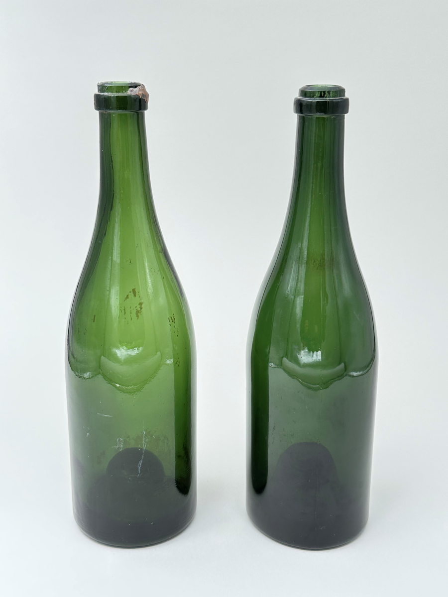 Buteljer, två stycken. Av grönt glas. Upphöjd botten, s.k. kinnekulle. 