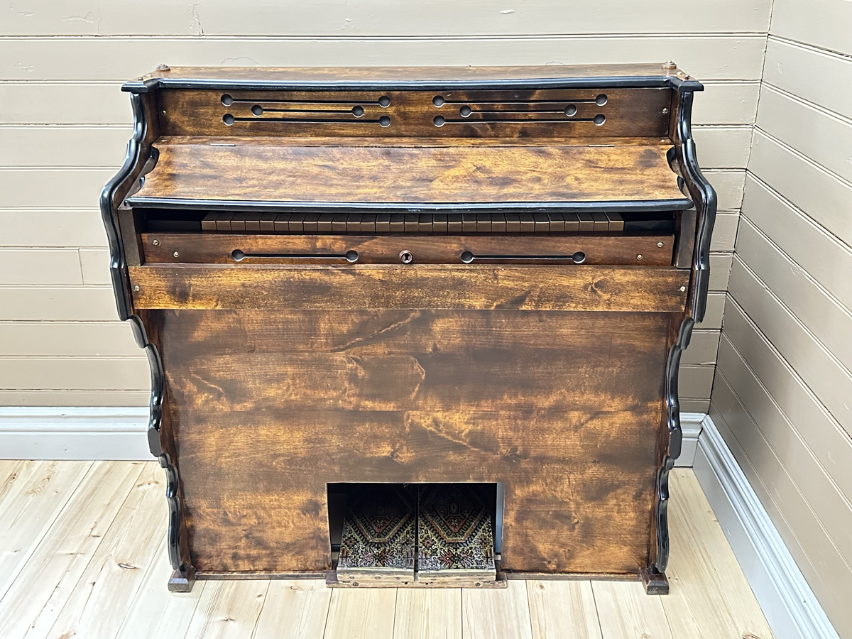 Orgel, tramporgel. Av mörk betsad och lackerad björk, samt svartmålad baksida. Profilerade sidostycken med målade svarta kanter. Dekorativt utformade ljudhål, som linjer med cirkulära avslut. Fäll- och låsbart lock med fastmonterad fällbar notställslist. Tangenter av trä med fanér på de vita tangenterna av ben el. horn. Två pedaler, klädda med sekundär, orientaliskt mönstrad och lackad korkmatta.