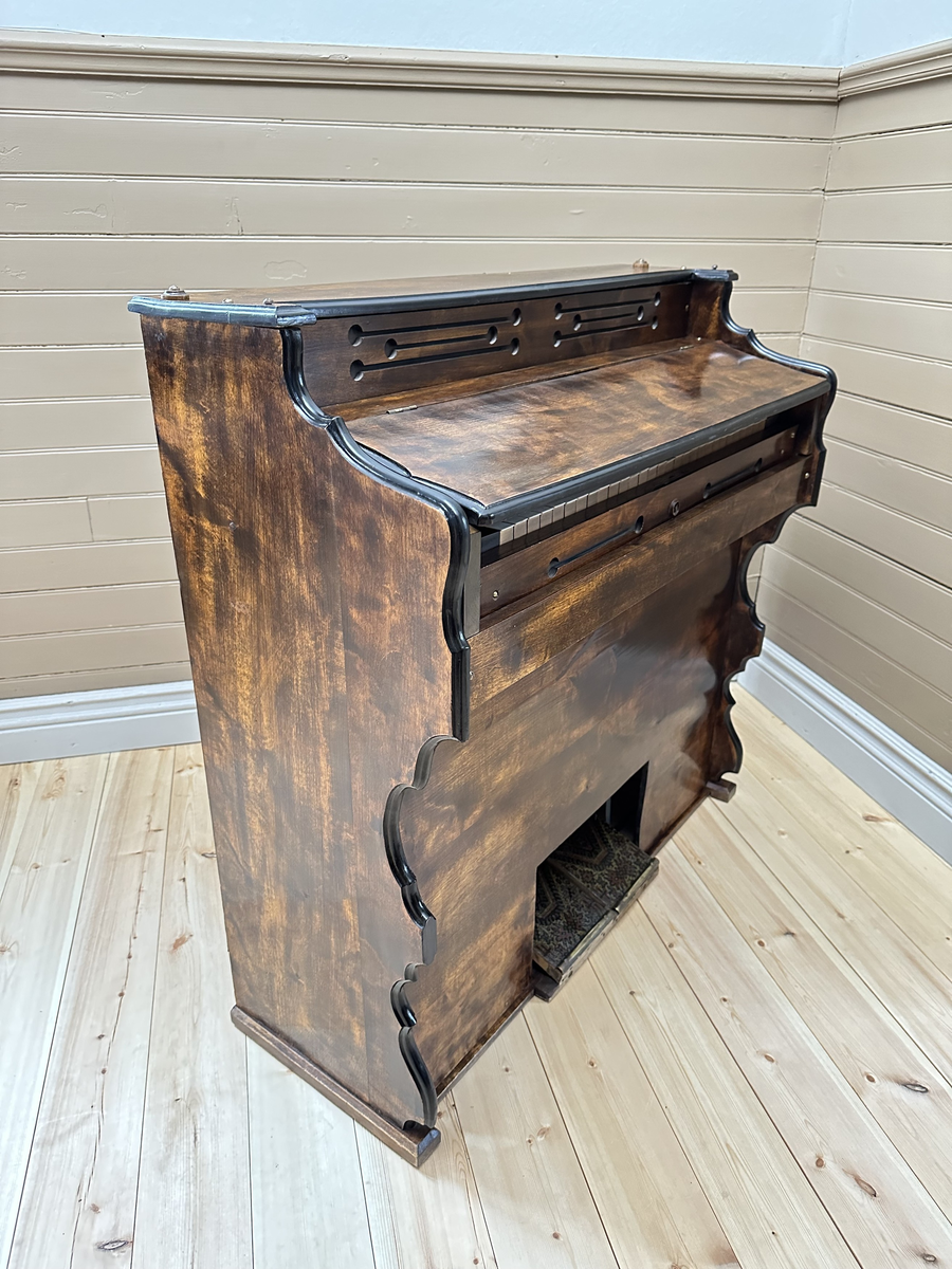 Orgel, tramporgel. Av mörk betsad och lackerad björk, samt svartmålad baksida. Profilerade sidostycken med målade svarta kanter. Dekorativt utformade ljudhål, som linjer med cirkulära avslut. Fäll- och låsbart lock med fastmonterad fällbar notställslist. Tangenter av trä med fanér på de vita tangenterna av ben el. horn. Två pedaler, klädda med sekundär, orientaliskt mönstrad och lackad korkmatta.