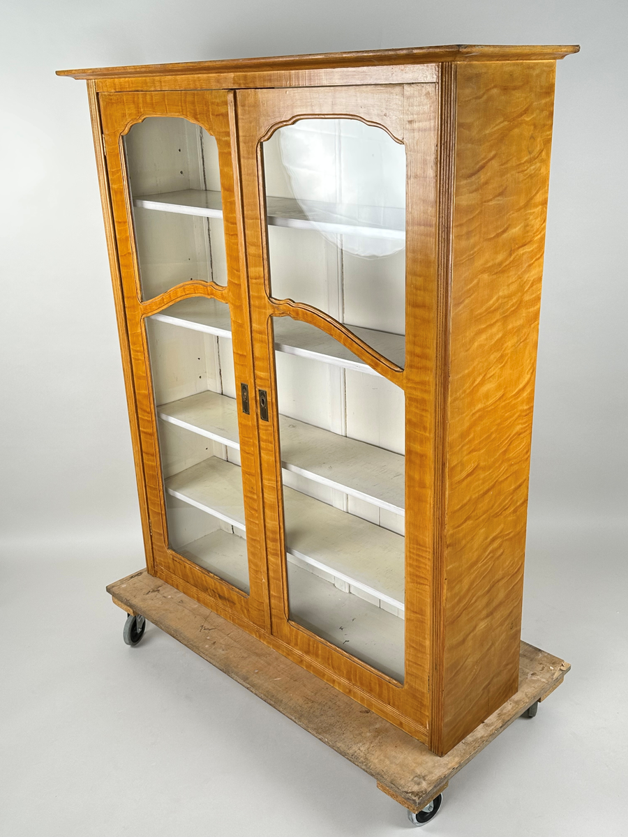 Materialskåp i trä, överskåp. Ådringsmålad i björkådring. Vitmålad på insidan. Två höga glasdörrar med två rutor vardera som skiljs åt vågrätt av en svängd list. De övre rutorna har en oval, något krusad överkant. Ena dörren med nyckelbricka i mässing. Räfflade fronter på skåpets sidostycken. Toppskiva profilerad undertill och överhängande.