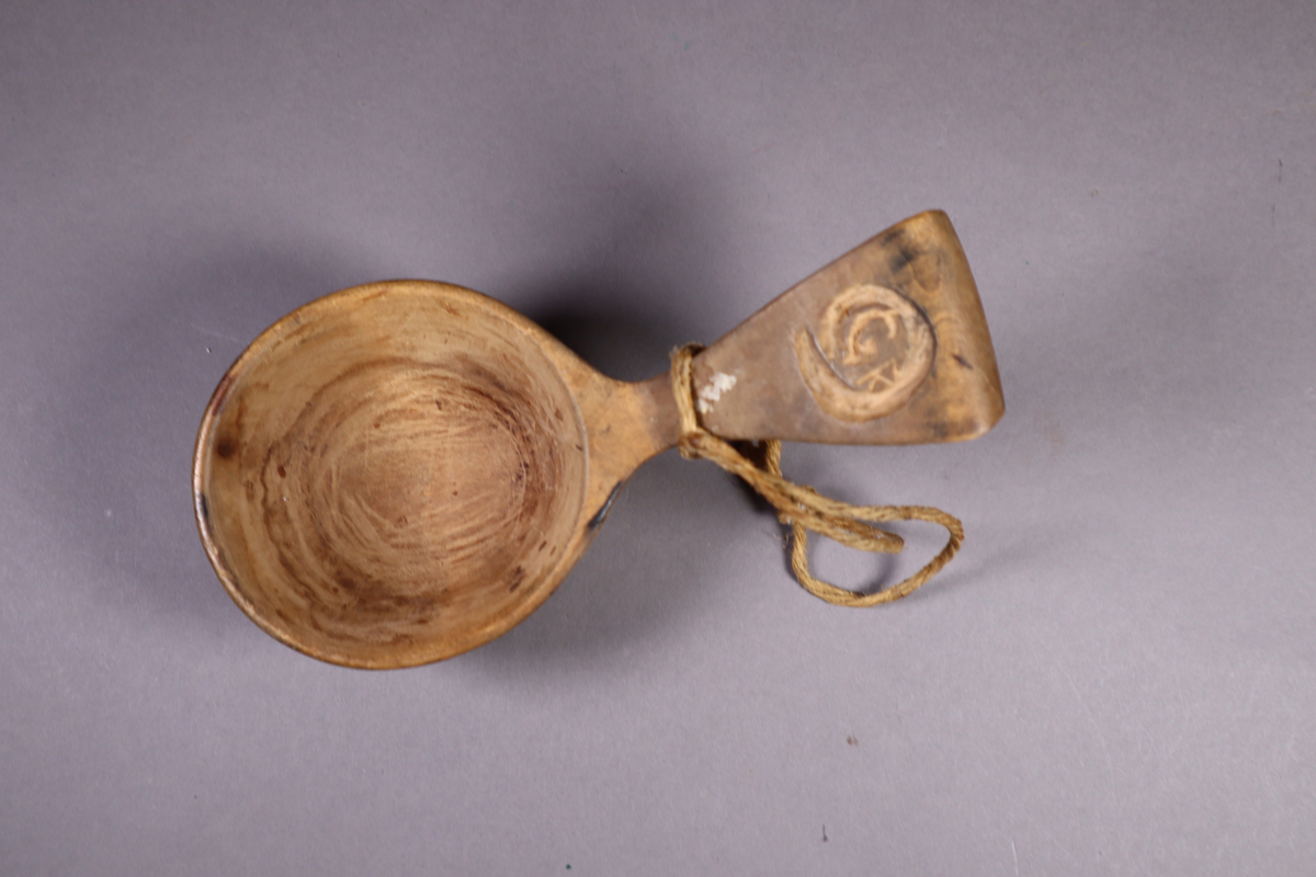 Trekopp med håndtakk som går skrått opp og avsluttes i en kort halvbue. Hyssing festet til håndtaket.