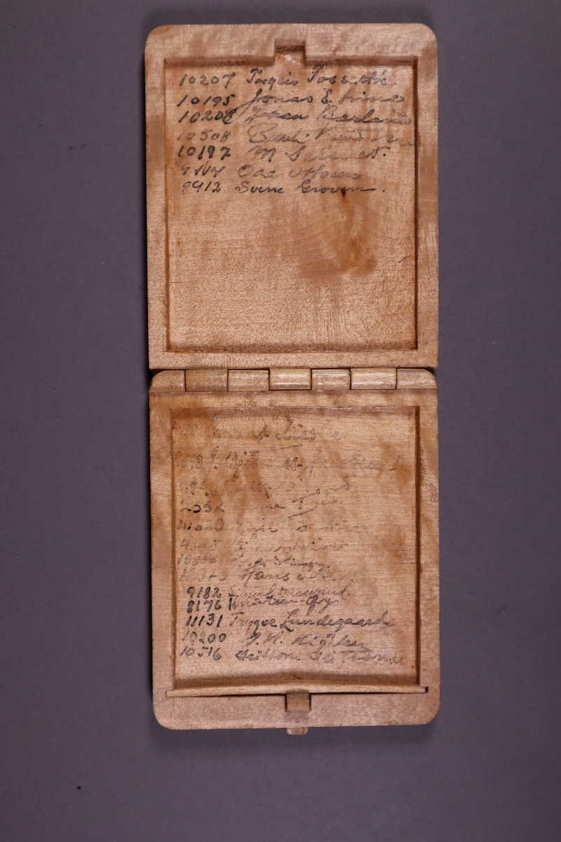 Etui med trengslet og uthuling inni med navn på fanger med fangenr. På fremsiden er det bilde av et tårn og et gjerde som må antas å være på Grini.