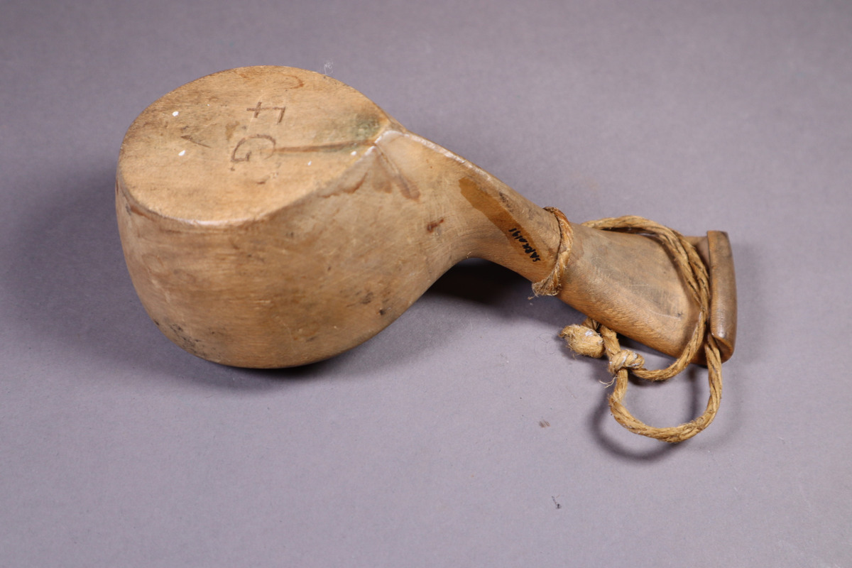 Trekopp med håndtakk som går skrått opp og avsluttes i en kort halvbue. Hyssing festet til håndtaket.