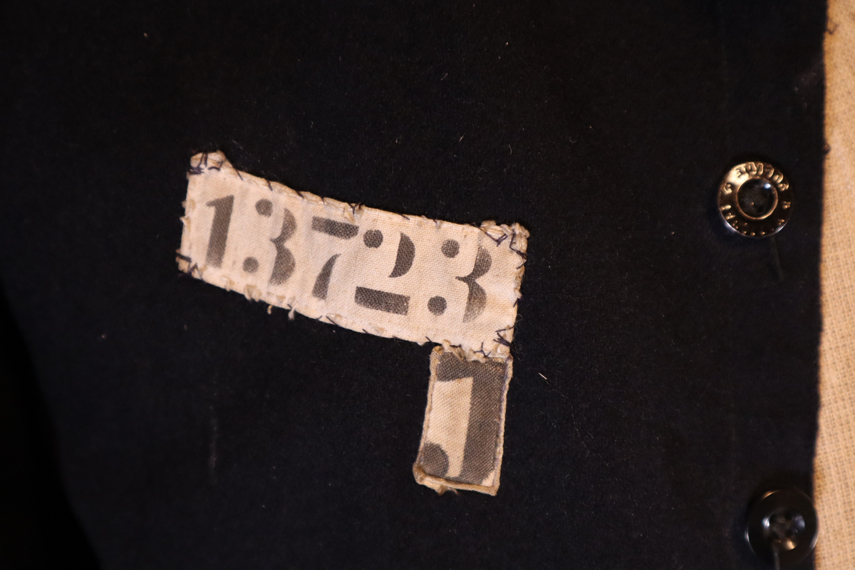 Fangejakke med påsydd lapp med fangenummer og bokstav.