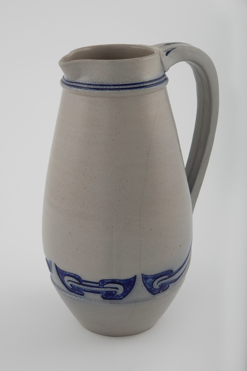 Kanne med grå bunn og koboltblå dekor. Kannen har stor buk. Dekoren er innskjært i leiren og fylt med koboltglasur. Dette gir effekten av dypt relieff. Jolly-dreid korpus. Håndtak er lagd separat. Kannen er glasert med saltglasur og dekoren med kobolt.