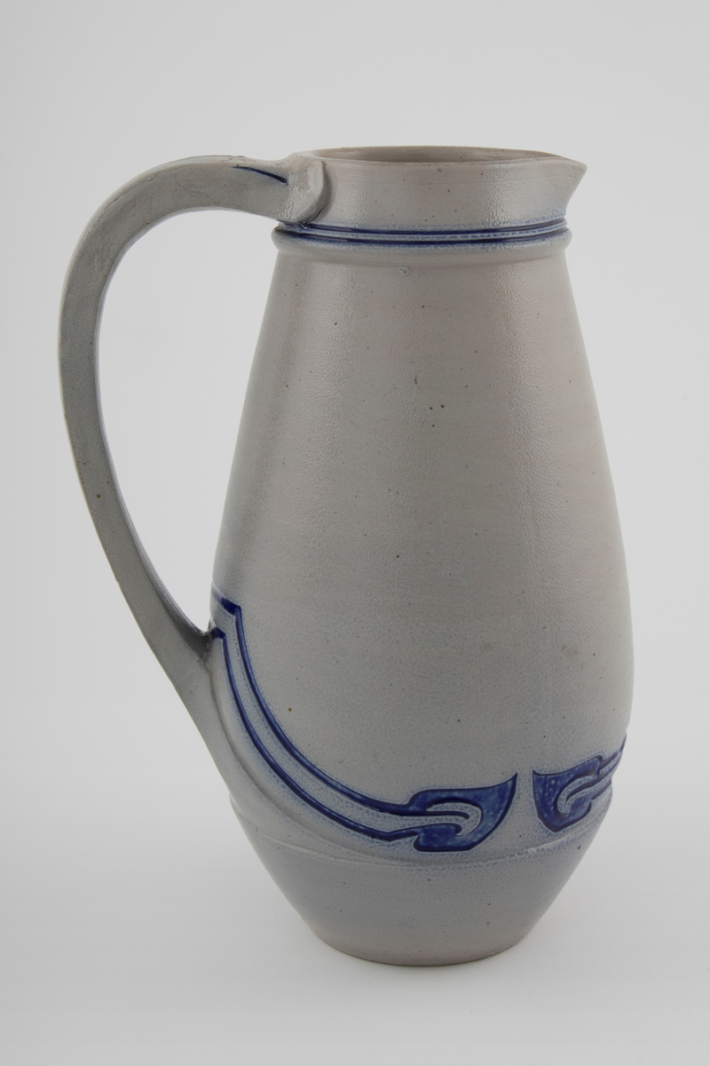 Kanne med grå bunn og koboltblå dekor. Kannen har stor buk. Dekoren er innskjært i leiren og fylt med koboltglasur. Dette gir effekten av dypt relieff. Jolly-dreid korpus. Håndtak er lagd separat. Kannen er glasert med saltglasur og dekoren med kobolt.