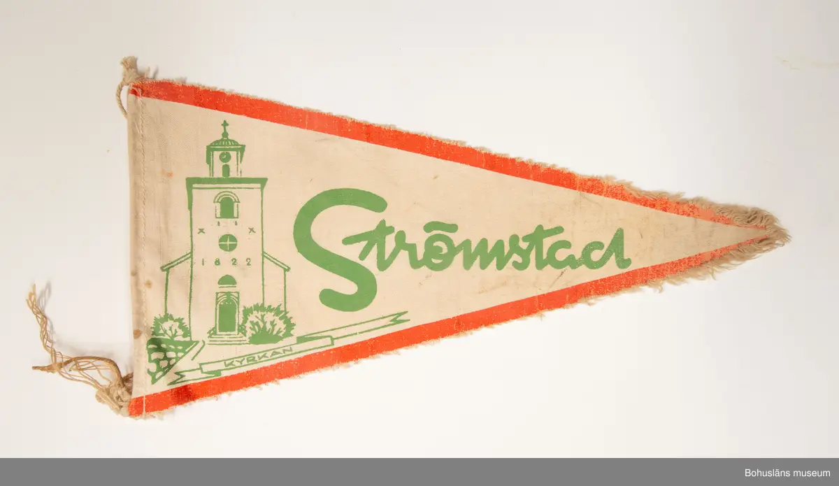Trekantig vimpel. Naturfärgad bomull med textiltryck. Röd kant och i grönt bild av Strömstads kyrka och namnet "Strömstad".
Sammanhör med UM026180 - UM026184.
Användar- och förvärvsuppgifter se UM026180