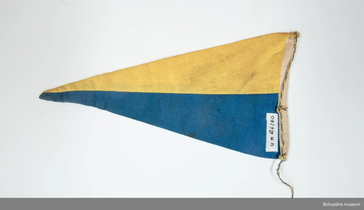 Fem vimplar (UM026180-UM026184) inköpta på semesterresa i Bohuslän 1960 då brukaren var 15 år. Han bodde med sina föräldrar i Stockholmstrakten där fadern var egen företagare med målerifirma. Att första semesterresan gick till Bohuslän  berodde till stor del på att fadern lärt känna en målarmästare från Uddevalla på en förgyllarkurs i Stockholm. Familjen skaffade 1957 en bil - Volkswagenbuss - som under veckorna användes i faderns firma och på helgerna med omgjord inredning av familjen för söndagsutflykter i Mälardalen.
Vid tiden för resan till Bohuslän var brukaren 15 år och arbetade som målarlärling och köpte vimplarna för egna intjänade pengar.
Vimplarna sattes fast på cykeln på snöre fäst nedtill på framgaffeln och andra ändan på styret,ett snöre på vardera sidan med där fastknutna vimplar som då fladdrade fint i fartvinden. Det var vanligt att  pojkarna tävlade att ha de mest ovanliga vimplarna med namn på olika platser (främst i Sverige), som verkade nästan exotiska. Cykelmotorcross var en vanliga företeelse. Brukaren bytte efter en kort tid cykeln mot NV-autoped (tidig mopedsort från Nymanverkstäderna i Uppsala). Vimplarna flyttades över till denna. Vimplar kunde även vara placerade bakom sitsen - "limpan" - på mopederna.
Den 12 augusti 1961 körde han in i sidan på en bil med sin trimmade autoped och skadades svårt. Efter denna dag har han ej använt vimplarna.
Flera av hans kamrater hade sådana vimplar uppsatta på väggarna i sina pojkrum, vilket brukaren aldrig haft.

Tresidig vimpel med ett övre gult och ett undre blått fält. Havsmotiv med fiskebåtar och namnet "Smögen" i svart textiltryck.
