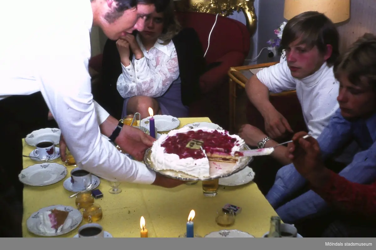 Tårtkalas hemma hos familjen Thörnqvist i Lindome, okänt årtal. Soffbordet är uppdukat med tända ljus och kaffeservice av finporslin. En man lutar sig fram över bordet och håller en tårta i händerna. Han bjuder två ungdomar att ta för sig.