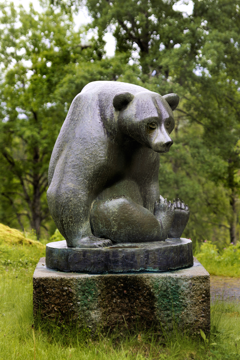 Vaksen bjørn i heilfigur av bronse på sokkel av granitt. Står i tunet på Grimdalen, Skafså.