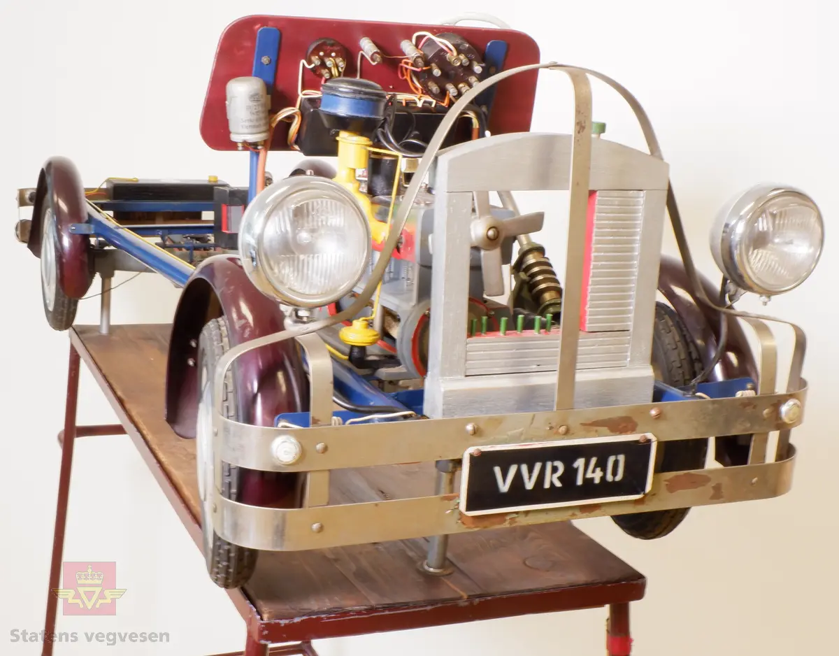Kjøreskolemodell i metall utformet som skjelettet av en bil. Det er tilkoblet lys og elektriske drivmotorer for å se bilen tekniske virkemåte.
Bilen har et medfølgende stativ for enklere å demonstrere utstyret for elever.
