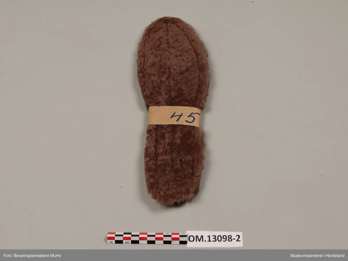 Rektangulær koffert av papp med beige, slangeskinnimitert utside og papirkledd innside. Hjørna er kledde med brune plastbeslag. Kofferten har to låsar og eit handtak av metall. Inni kofferten er 40 par med innleggssolar av saueskinn i ulike storleikar og fargar.