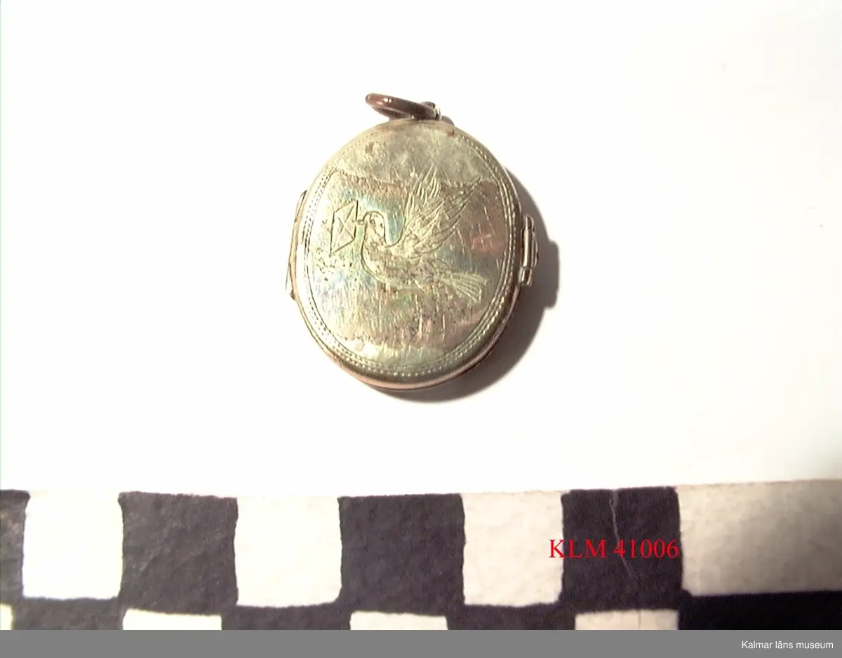 KLM 41006 Medaljong, metall. Utsidan med graverad dekor, bl a en brevduva. Inuti fotografier av Stina Wimmerströms farföräldrar, Carolina och Carl Wimmerström.