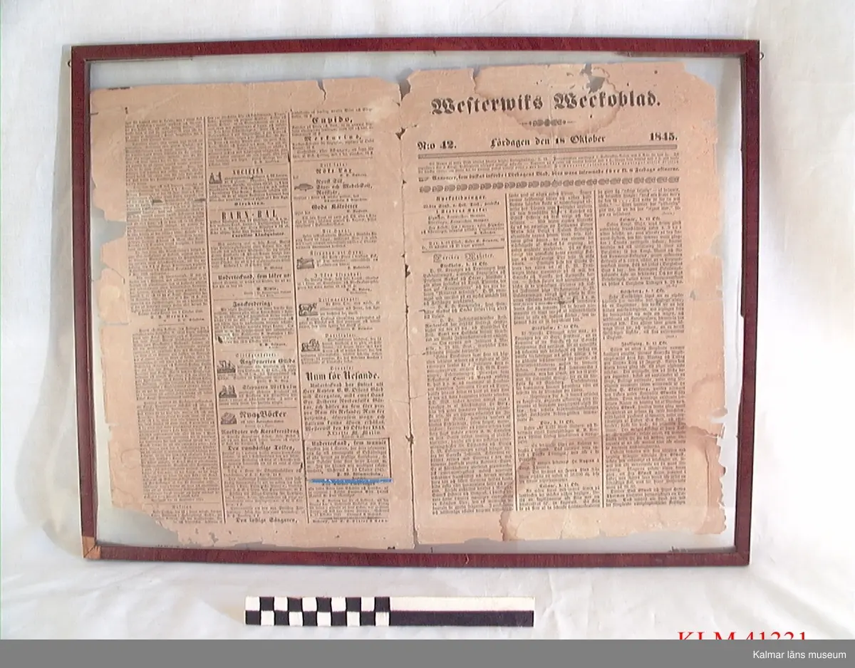 KLM 41331 Tidning, papper. Fyrsidigt tryck utvikt och inramat bakom glas i brun träram. Westerwiks Weckoblad från lördagen den 18 oktober 1845. På sista sidan är en annons markerad där konditor F.W. Wimmerström erbjuder sina tjänster. Fredrik Wilhelm Wimmerström var Stina Wimmerströms farfarsfar.