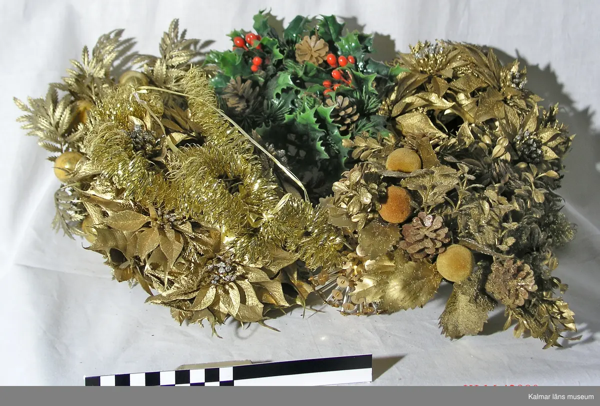 KLM 42980 Julprydnad, 5 st, plast. Kransar tillverkade av olika plastdetaljer som blommor, blad, kulor m.m. i guldfärg och grönt, samt tallkottar. Att hänga upp.