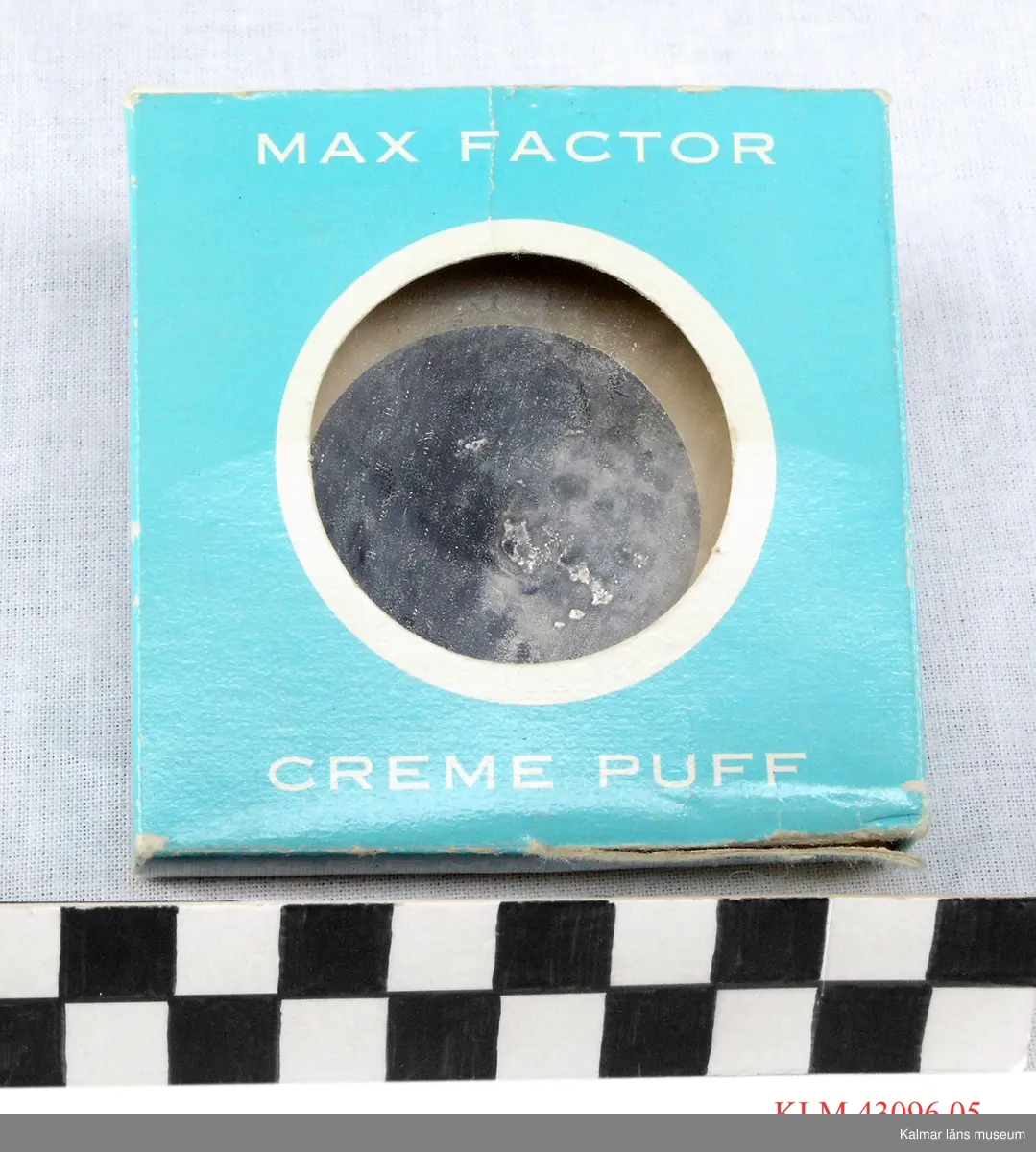 KLM 43096:5 Puderdosa. Rund dosa av metall med spegel. I kvadratisk förpackning av blått papper, text i vitt "MAX FACTOR CREME PUFF".