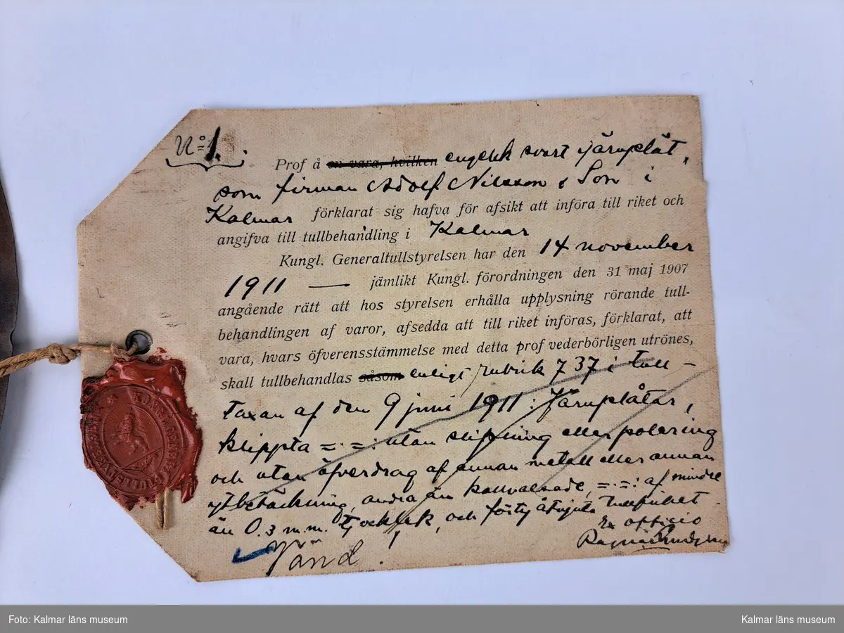 KLM 46816:1:1-2. Varuprov, järnplåt, 2 st. Två runda järnplåtar. :1. Med lapp i snöre, fäst genom hål i plåten. På lappen tryckt och handskriven text i svart på framsidan, handskriven text på baksidan samt en röd sigillstämpel. Text stämpel: Kongl Generaltullstyrelsen. På lappen handskrivet nummer: Stat. nr 1412. Påskrift plåt: ? 9157 1911. :2. En påklistad vit etikett samt påskrift plåt: Stat.nr.