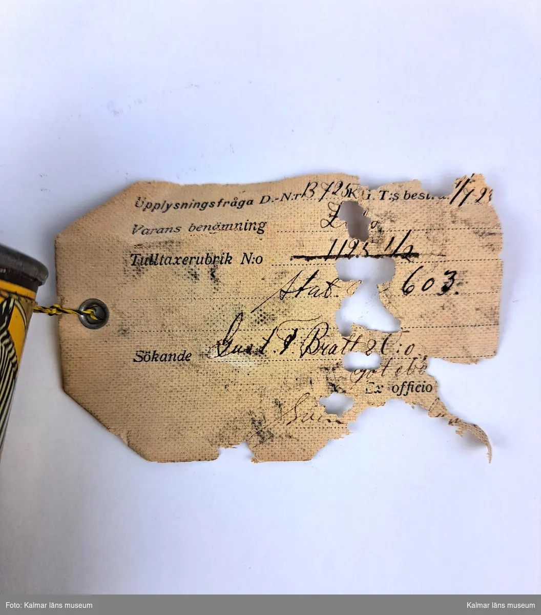 KLM 46816:16. Varuprov, förpackning. Rund metallburk med färgtryck och bild på en zebra. Trasig botten. Text: Zebo Flytande ugnssvärta, För svärtning av ugnar, spisar, järnstaket etc. Vit lapp/etikett, delvis trasig, hängande i textiltråd med tryckt och handskriven text (delvis otydlig): Stat. 603, Gust. T? Bratt & Co Göteborg (troligtvis). Handskriven text på baksidan samt en röd sigillstämpel. Text stämpel: Kongl Generaltullstyrelsen.