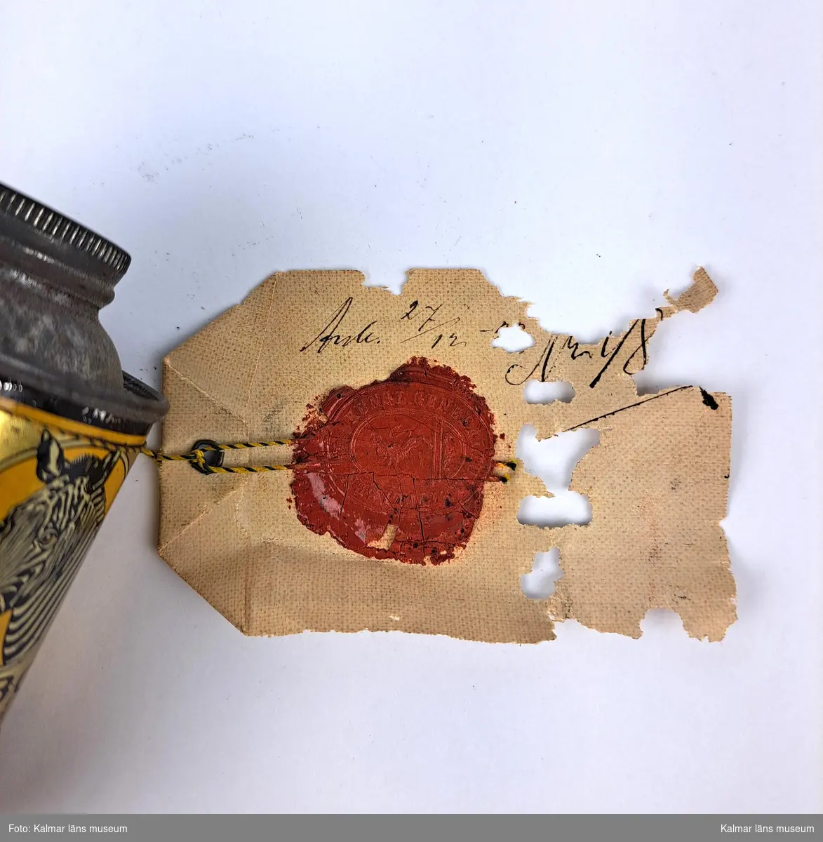 KLM 46816:16. Varuprov, förpackning. Rund metallburk med färgtryck och bild på en zebra. Trasig botten. Text: Zebo Flytande ugnssvärta, För svärtning av ugnar, spisar, järnstaket etc. Vit lapp/etikett, delvis trasig, hängande i textiltråd med tryckt och handskriven text (delvis otydlig): Stat. 603, Gust. T? Bratt & Co Göteborg (troligtvis). Handskriven text på baksidan samt en röd sigillstämpel. Text stämpel: Kongl Generaltullstyrelsen.