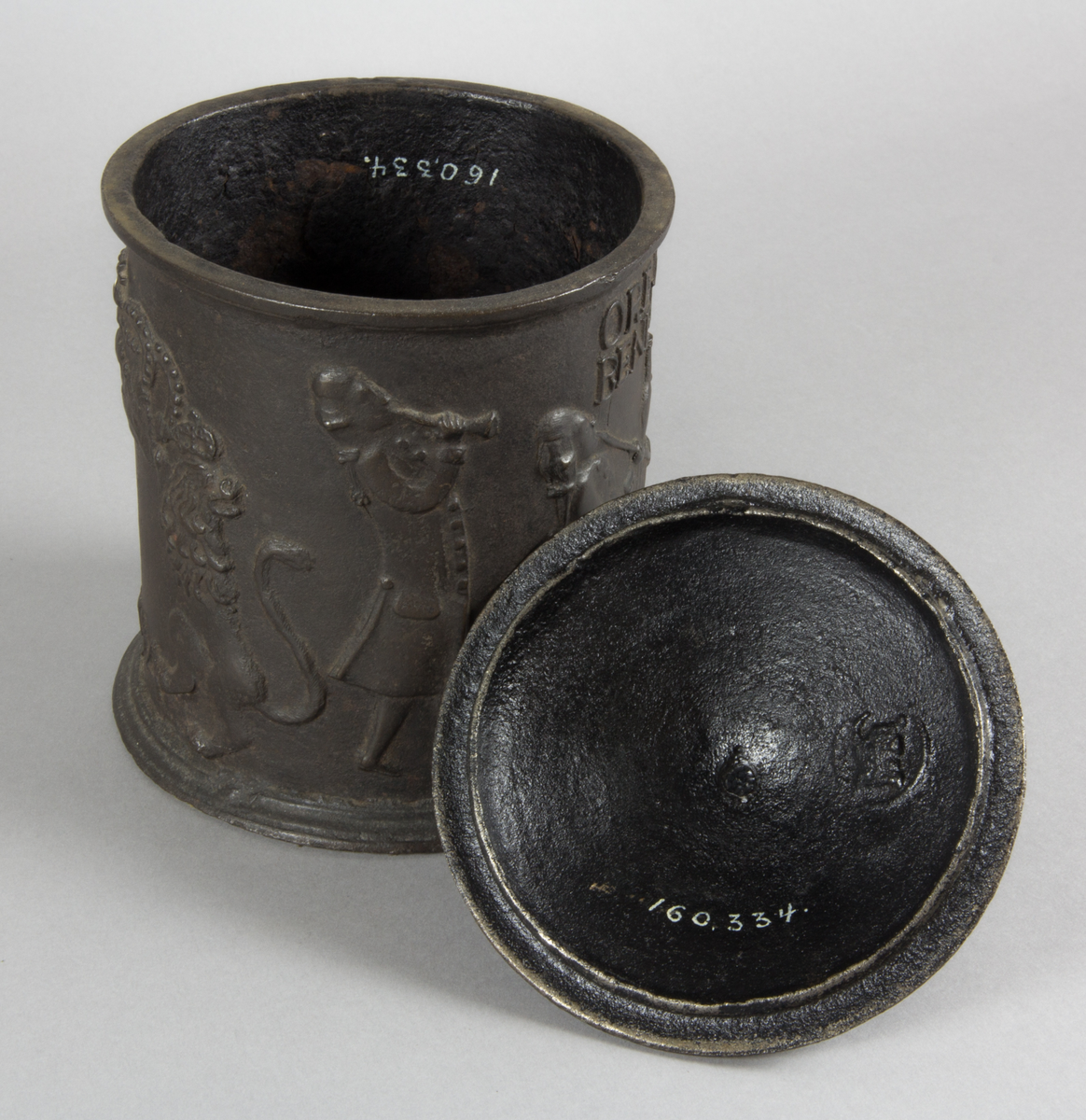 Relief på burken med text. Relief med rökande och spelande män. Några av männen sitter vid en spis. Riksvapen med flankerande lejon. Årtal 1794.
Text på burken. ORE FUMOSO BENE BIBENTUR.