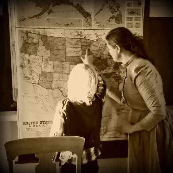 sepiafarga bilde med kvinneleg lærar i kjole og lyshåra gut som ser på kart over USA