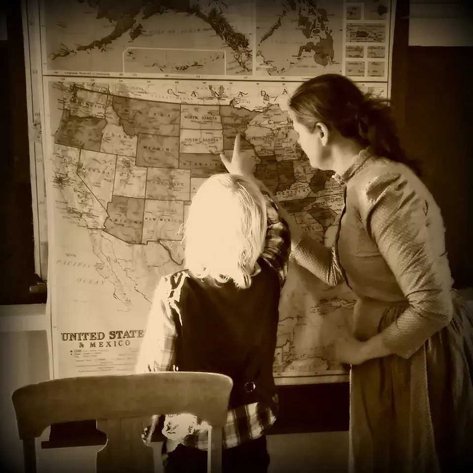 sepiafarga bilde med kvinneleg lærar i kjole og lyshåra gut som ser på kart over USA