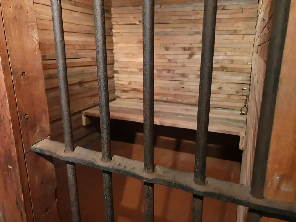 Gitter i jern inn mot fengselscelle med trebenk