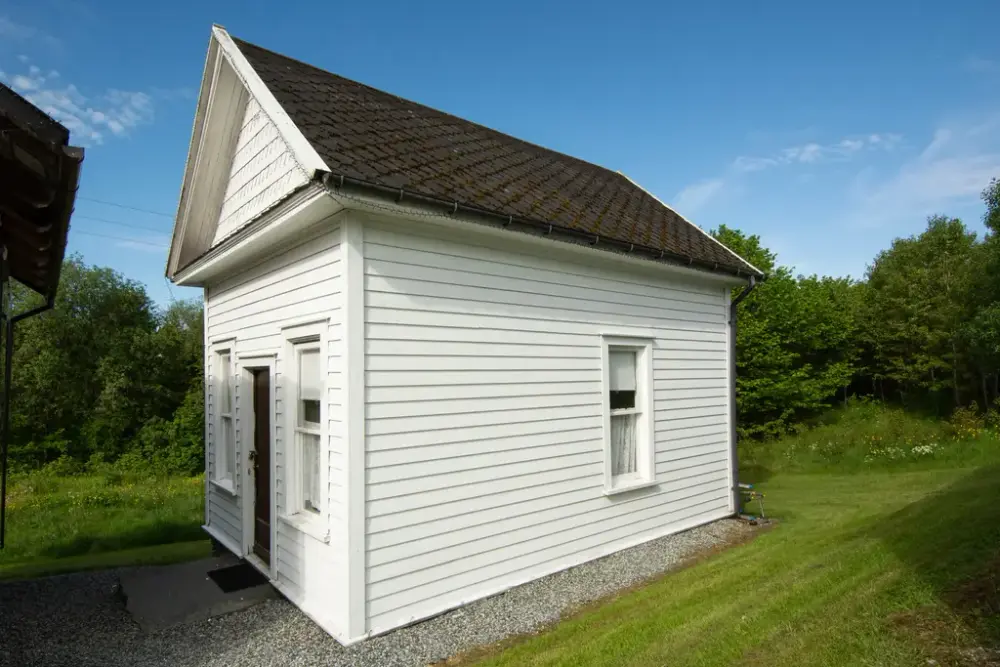 Kvitt hus, en etasje med dør og to vinduer på kortsiden og et vindu på langsiden