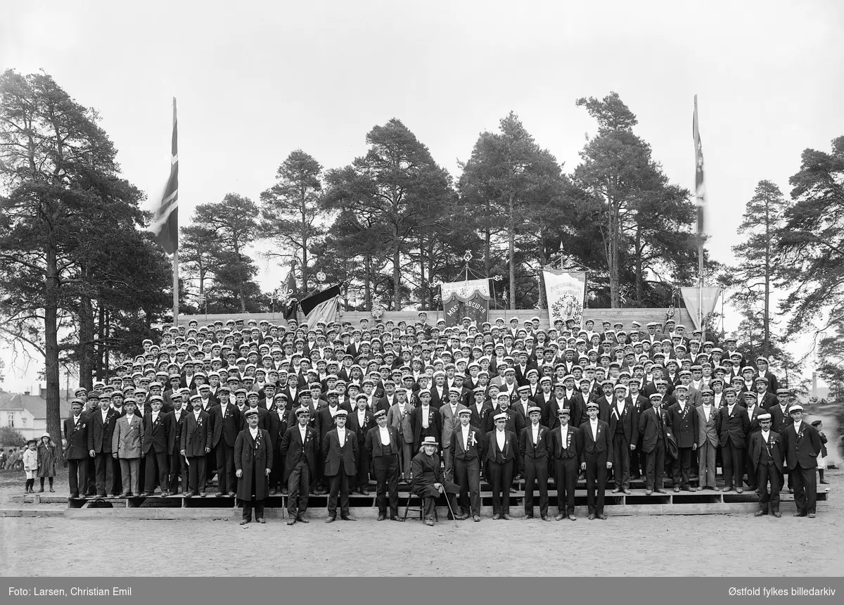 Stor gruppe fotografert i amfiet i Kulås-parken i Sarpsborg, antakelig fra sangerstevne. Mannskor.
Fane med Moss arbeider... og Fagforeningskoret Sarpsborg (ant.).
To unge linselus til venstre i bildet. 
Antakelig dirigenter i forgrunnen. Sittende på en stol foran i midten, dirigent og komponist Christian Haslerud.