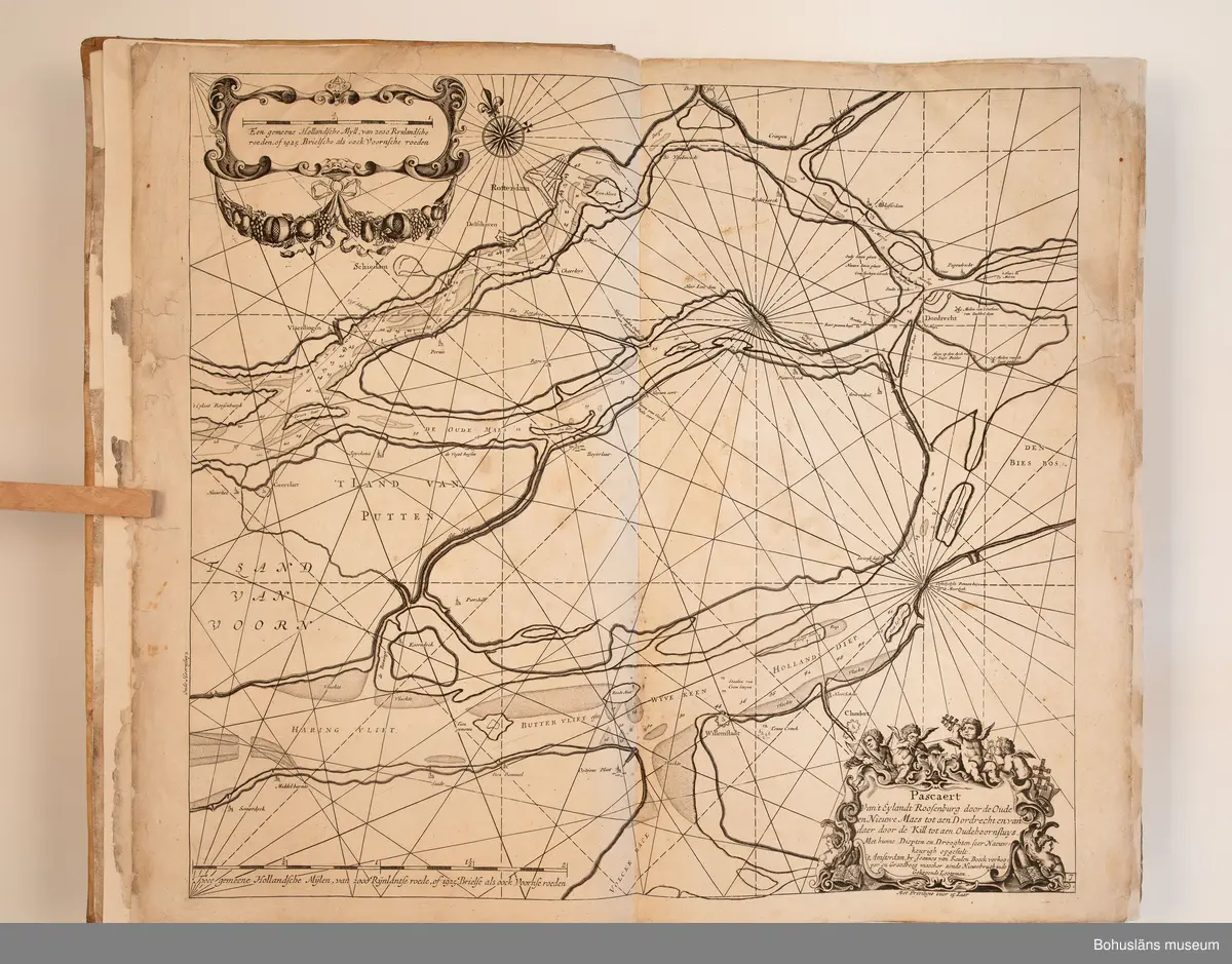 Holländskt sjökort i två sammanbundna delar, tryckta 1697 i Amsterdam.
Brunt skinnband av pergament i relativt gott skick med upphöjda bind. Text på nederlänska  i frakturstil med rikt illustrerade kartblad, ofta utvikbara. Restaurerad hos papperskonservator. 

Handanteckningar på pärmsidans insida:  
William Andrew Macfie 
Anfasteröd.
Till museum 14/9 64

Tryckt text på titelbladet första delen: 
De nieuwe groote lichtende zee-fackel, ´t derde deel. Verthoonende de kulten van Granada, Catalonien, Provence, Italien, Dalmatien, Grieken, Thracien, Anatolien, Syrien, Egypten, en de geheele noordkust van Barbaryen, met alle haer onderbehoorende en ... leggende eylanden. Als mede de beschrijvingh van alle havenen, bayen, reeden, drooghten, diepten, streckingen en opdoeningen van landen. Op de ware pools hoogte geleyd. Uyt ondervindinge van veel ervarene stuurlieden, lootsen en liefhebbers der zeevaert, vergadert door Claas Jansz. Vooght ... – 

T´Amsteldam, gedruckt by Joannes van Keulen, boeck-en zee-kaert-verkoper, aen de Nieuw-brugh, in de gekroonde lootsman, 1697, 1697 - 4], 29 s., s. 26, s. 31-92, s. 1-22, s. 1-20, [80] pl.-bl : kartor

Tryckt på titelbladet andra delen:
De nieuwe groote lichtende zee-fakkel, ´t tweede deel. Verthoonende de zee-kusten van het zyderste gedeelte van de Noord-zee, ´t Canaal, ´t westersche gedeelte van Engeland en Schotland, Yrland, Vrankrijk, Spanjen, Marocco, Gualata, Genehoa en Gambia, met de onder-vehoorige eylanden,mitsgaders ve vlaamsche, canarische en soute Eylanden. Als mede de ... van alle havenen, bayen, reeden, droogten, diepten, streckingen en opdoeningen van landen, op de ware pools hoogte geleyd, uptonderbindinge van veele ervarene stuurlieden, lootsen en lief-hebbers der zee-vaart. Zijnde van alle ... door Claes Jansz. Vooght ... - T´Amsterdam, gedrukt by Joannes van Keulen, boek zee-kaart-verkooper, en graadboogmaker aan de oost-zyde van de Nieuw-brug, in de gekroonde lootsman, 169.., 169n - 4], 4 s., s. 7-34, s. 53, s. 36, s. 35, s. 38, s. 35, s. 40-85, s. 68, s. 87-91, s. 29, s. 93-97, [87] pl.-bl : kartor