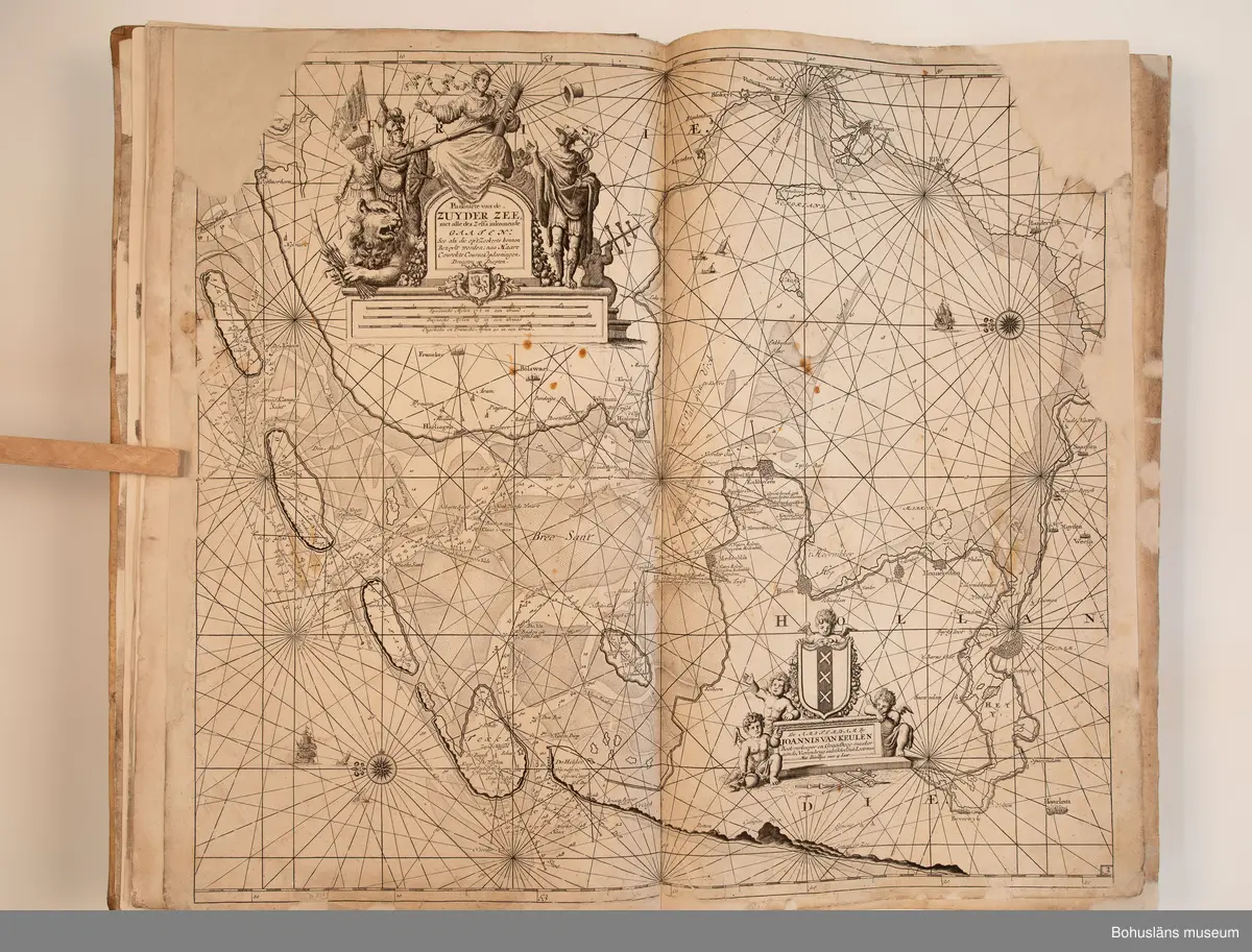 Holländskt sjökort i två sammanbundna delar, tryckta 1697 i Amsterdam.
Brunt skinnband av pergament i relativt gott skick med upphöjda bind. Text på nederlänska  i frakturstil med rikt illustrerade kartblad, ofta utvikbara. Restaurerad hos papperskonservator. 

Handanteckningar på pärmsidans insida:  
William Andrew Macfie 
Anfasteröd.
Till museum 14/9 64

Tryckt text på titelbladet första delen: 
De nieuwe groote lichtende zee-fackel, ´t derde deel. Verthoonende de kulten van Granada, Catalonien, Provence, Italien, Dalmatien, Grieken, Thracien, Anatolien, Syrien, Egypten, en de geheele noordkust van Barbaryen, met alle haer onderbehoorende en ... leggende eylanden. Als mede de beschrijvingh van alle havenen, bayen, reeden, drooghten, diepten, streckingen en opdoeningen van landen. Op de ware pools hoogte geleyd. Uyt ondervindinge van veel ervarene stuurlieden, lootsen en liefhebbers der zeevaert, vergadert door Claas Jansz. Vooght ... – 

T´Amsteldam, gedruckt by Joannes van Keulen, boeck-en zee-kaert-verkoper, aen de Nieuw-brugh, in de gekroonde lootsman, 1697, 1697 - 4], 29 s., s. 26, s. 31-92, s. 1-22, s. 1-20, [80] pl.-bl : kartor

Tryckt på titelbladet andra delen:
De nieuwe groote lichtende zee-fakkel, ´t tweede deel. Verthoonende de zee-kusten van het zyderste gedeelte van de Noord-zee, ´t Canaal, ´t westersche gedeelte van Engeland en Schotland, Yrland, Vrankrijk, Spanjen, Marocco, Gualata, Genehoa en Gambia, met de onder-vehoorige eylanden,mitsgaders ve vlaamsche, canarische en soute Eylanden. Als mede de ... van alle havenen, bayen, reeden, droogten, diepten, streckingen en opdoeningen van landen, op de ware pools hoogte geleyd, uptonderbindinge van veele ervarene stuurlieden, lootsen en lief-hebbers der zee-vaart. Zijnde van alle ... door Claes Jansz. Vooght ... - T´Amsterdam, gedrukt by Joannes van Keulen, boek zee-kaart-verkooper, en graadboogmaker aan de oost-zyde van de Nieuw-brug, in de gekroonde lootsman, 169.., 169n - 4], 4 s., s. 7-34, s. 53, s. 36, s. 35, s. 38, s. 35, s. 40-85, s. 68, s. 87-91, s. 29, s. 93-97, [87] pl.-bl : kartor