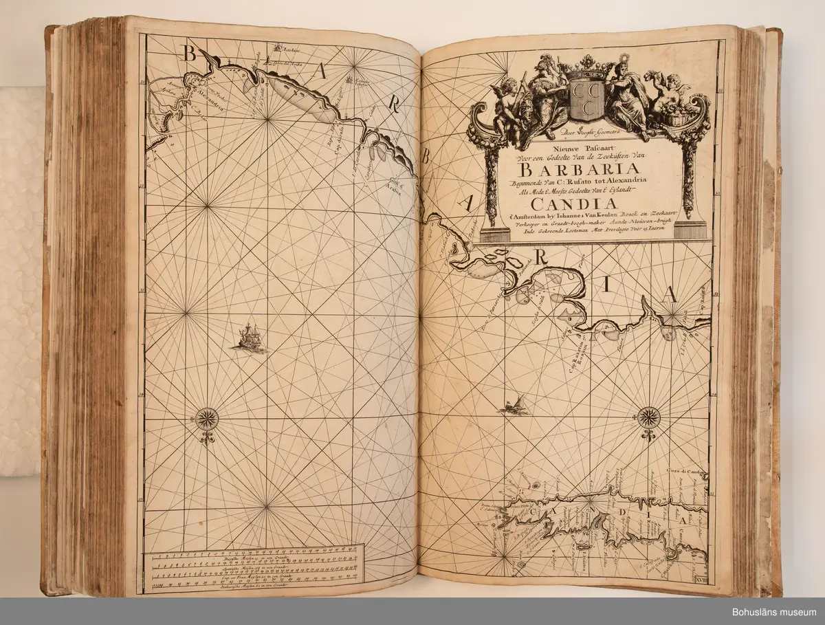Holländskt sjökort i två sammanbundna delar, tryckta 1697 i Amsterdam.
Brunt skinnband av pergament i relativt gott skick med upphöjda bind. Text på nederlänska  i frakturstil med rikt illustrerade kartblad, ofta utvikbara. Restaurerad hos papperskonservator. 

Handanteckningar på pärmsidans insida:  
William Andrew Macfie 
Anfasteröd.
Till museum 14/9 64

Tryckt text på titelbladet första delen: 
De nieuwe groote lichtende zee-fackel, ´t derde deel. Verthoonende de kulten van Granada, Catalonien, Provence, Italien, Dalmatien, Grieken, Thracien, Anatolien, Syrien, Egypten, en de geheele noordkust van Barbaryen, met alle haer onderbehoorende en ... leggende eylanden. Als mede de beschrijvingh van alle havenen, bayen, reeden, drooghten, diepten, streckingen en opdoeningen van landen. Op de ware pools hoogte geleyd. Uyt ondervindinge van veel ervarene stuurlieden, lootsen en liefhebbers der zeevaert, vergadert door Claas Jansz. Vooght ... – 

T´Amsteldam, gedruckt by Joannes van Keulen, boeck-en zee-kaert-verkoper, aen de Nieuw-brugh, in de gekroonde lootsman, 1697, 1697 - 4], 29 s., s. 26, s. 31-92, s. 1-22, s. 1-20, [80] pl.-bl : kartor

Tryckt på titelbladet andra delen:
De nieuwe groote lichtende zee-fakkel, ´t tweede deel. Verthoonende de zee-kusten van het zyderste gedeelte van de Noord-zee, ´t Canaal, ´t westersche gedeelte van Engeland en Schotland, Yrland, Vrankrijk, Spanjen, Marocco, Gualata, Genehoa en Gambia, met de onder-vehoorige eylanden,mitsgaders ve vlaamsche, canarische en soute Eylanden. Als mede de ... van alle havenen, bayen, reeden, droogten, diepten, streckingen en opdoeningen van landen, op de ware pools hoogte geleyd, uptonderbindinge van veele ervarene stuurlieden, lootsen en lief-hebbers der zee-vaart. Zijnde van alle ... door Claes Jansz. Vooght ... - T´Amsterdam, gedrukt by Joannes van Keulen, boek zee-kaart-verkooper, en graadboogmaker aan de oost-zyde van de Nieuw-brug, in de gekroonde lootsman, 169.., 169n - 4], 4 s., s. 7-34, s. 53, s. 36, s. 35, s. 38, s. 35, s. 40-85, s. 68, s. 87-91, s. 29, s. 93-97, [87] pl.-bl : kartor