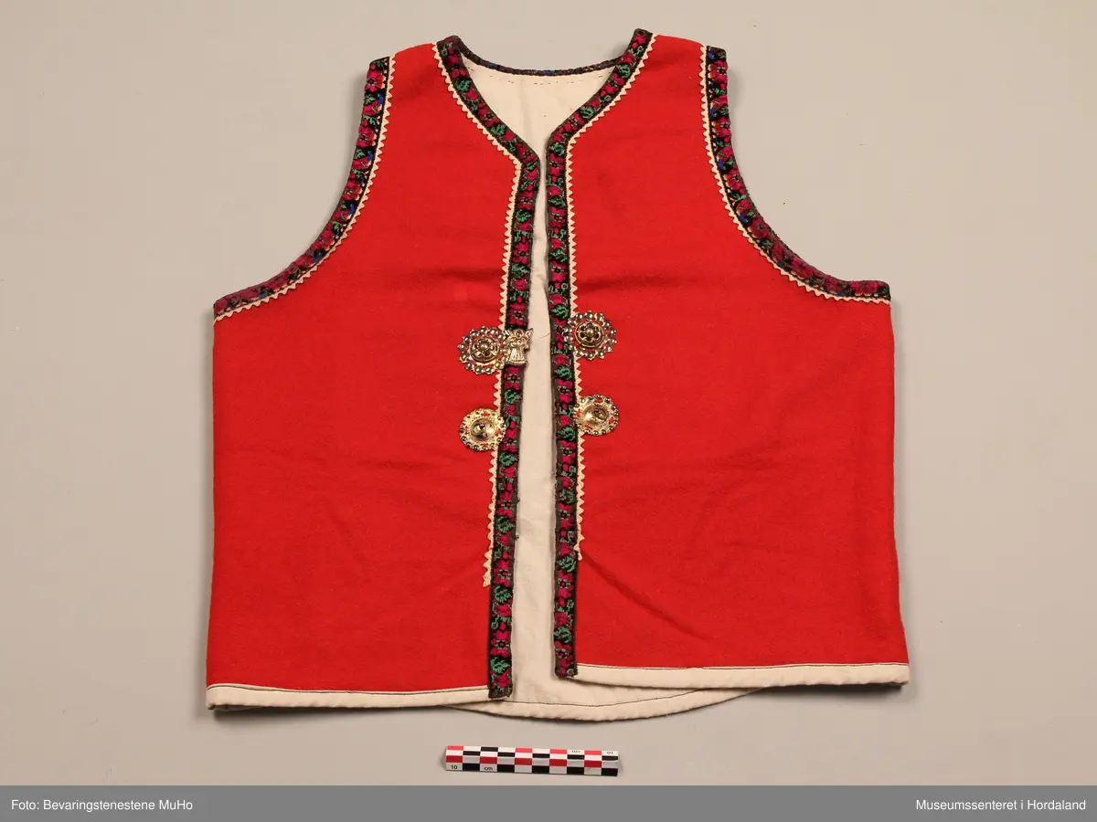 Liv i raudt ullstoff, med rosekvarding rundt opningane. Kvit krokalisse i bomull innom. Livet har tett skjering rundt halsen. Ubleika lerretfor i bomull. På kvar side av frontopninga er det ein bore med ring i midten, ovenfor desse er det ei jomfruspenne med engel i midten. Alle desse er i forgylt sølv. To saum i sidene. To hekter nede på livet til attlat, og tre hekter nede på ryggen. Foret kjem fram på framsida og danner ein kant nedst på livet.