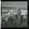 En man i ljus basker står framför ett sommarhus med sin cykel lastad med väskor. På pakethållaren sitter en flicka.