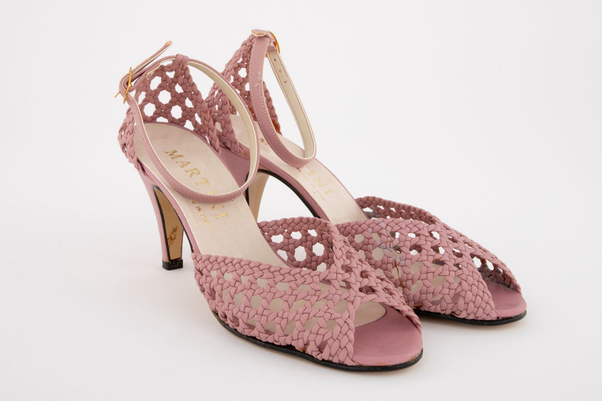 Rottingflettet selskapssandeler med ankelstropp, åpen tå og stiletthæl. Både hælkappe og forblad er utført i kurvfletting, mens hæl og ankelstropp er i glatt skinn. Ankelstroppen reguleres med på yttersiden med spenne av gullfarget metall. Innvendig fôret med blek syrinfarget, imitert skinn, før påføring av et ytre lag med kremfarget, imitert skinn. Kun den åpne tåen er fortsatt syrinfarget. Både overside og såle er av syntetmaterilale. Str. 37. Sålen er av naturfarget, glatt lærimitasjon, med svartmalt ytterkant.

Originaleske følger med, se NK2002-206-002