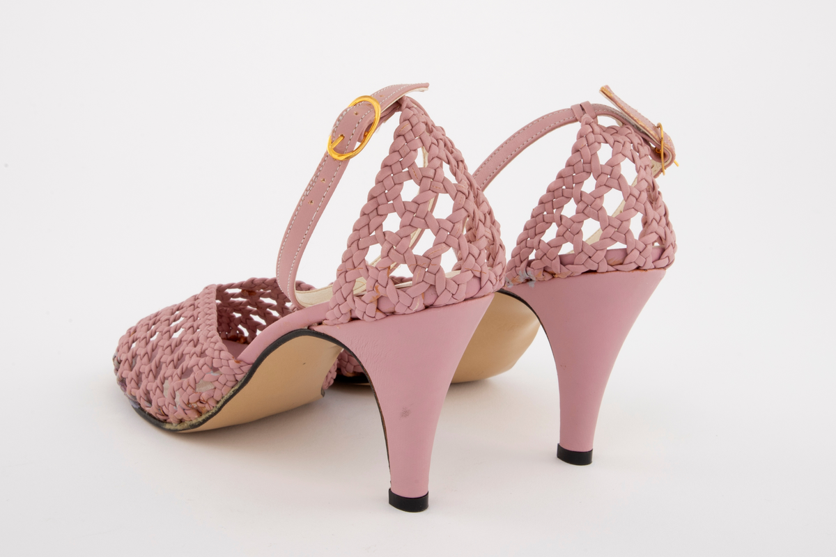 Rottingflettet selskapssandeler med ankelstropp, åpen tå og stiletthæl. Både hælkappe og forblad er utført i kurvfletting, mens hæl og ankelstropp er i glatt skinn. Ankelstroppen reguleres med på yttersiden med spenne av gullfarget metall. Innvendig fôret med blek syrinfarget, imitert skinn, før påføring av et ytre lag med kremfarget, imitert skinn. Kun den åpne tåen er fortsatt syrinfarget. Både overside og såle er av syntetmaterilale. Str. 37. Sålen er av naturfarget, glatt lærimitasjon, med svartmalt ytterkant.

Originaleske følger med, se NK2002-206-002