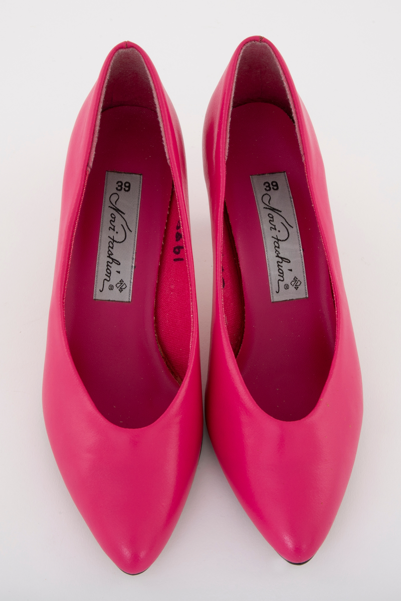 Sjokkrosa pumps med moderat høy stiletthæl. Syntetskinn, fôret med tekstil, alt sterkt rosa. Lys beige syntetsåle og svart plastflikk. Både ringning og tå er ganske spisse. Ingen synlig søm på utsiden av ringningen. Polstret binnsåle, dvs en mellomsåle av skumgummi. Str. 39
