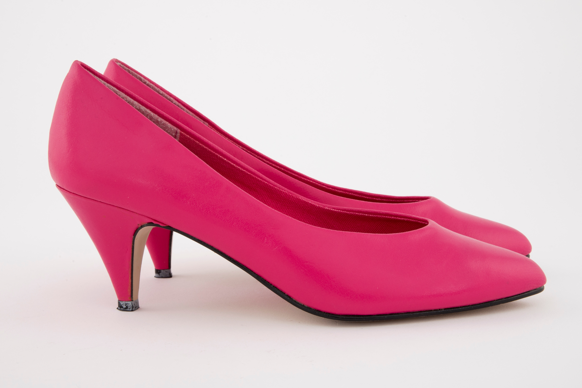 Sjokkrosa pumps med moderat høy stiletthæl. Syntetskinn, fôret med tekstil, alt sterkt rosa. Lys beige syntetsåle og svart plastflikk. Både ringning og tå er ganske spisse. Ingen synlig søm på utsiden av ringningen. Polstret binnsåle, dvs en mellomsåle av skumgummi. Str. 39